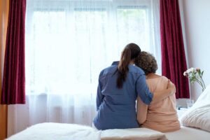 An adult child gently helping an older parent stand up from a chair in a cozy living room.