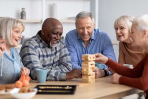 Older adults and caregivers talking in a bright, comfortable common room with seating and large windows.